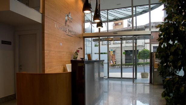 Zona de recepción de un hotel con un mostrador de madera, puerta de cristal de entrada y vista a la calle.