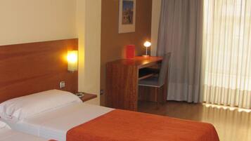 A hotel room with two beds, a desk, a chair, a nightstand, an air conditioning unit, and a window with curtains.