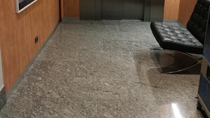 Un pasillo con pared de madera, un cuadro abstracto enmarco, suelo de mármol y un banco de cuero negro.