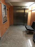 Un pasillo con pared de madera, un cuadro abstracto enmarco, suelo de mármol y un banco de cuero negro.