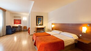 Habitación de hotel con dos camas, un escritorio, una silla y un cuadro en la pared.