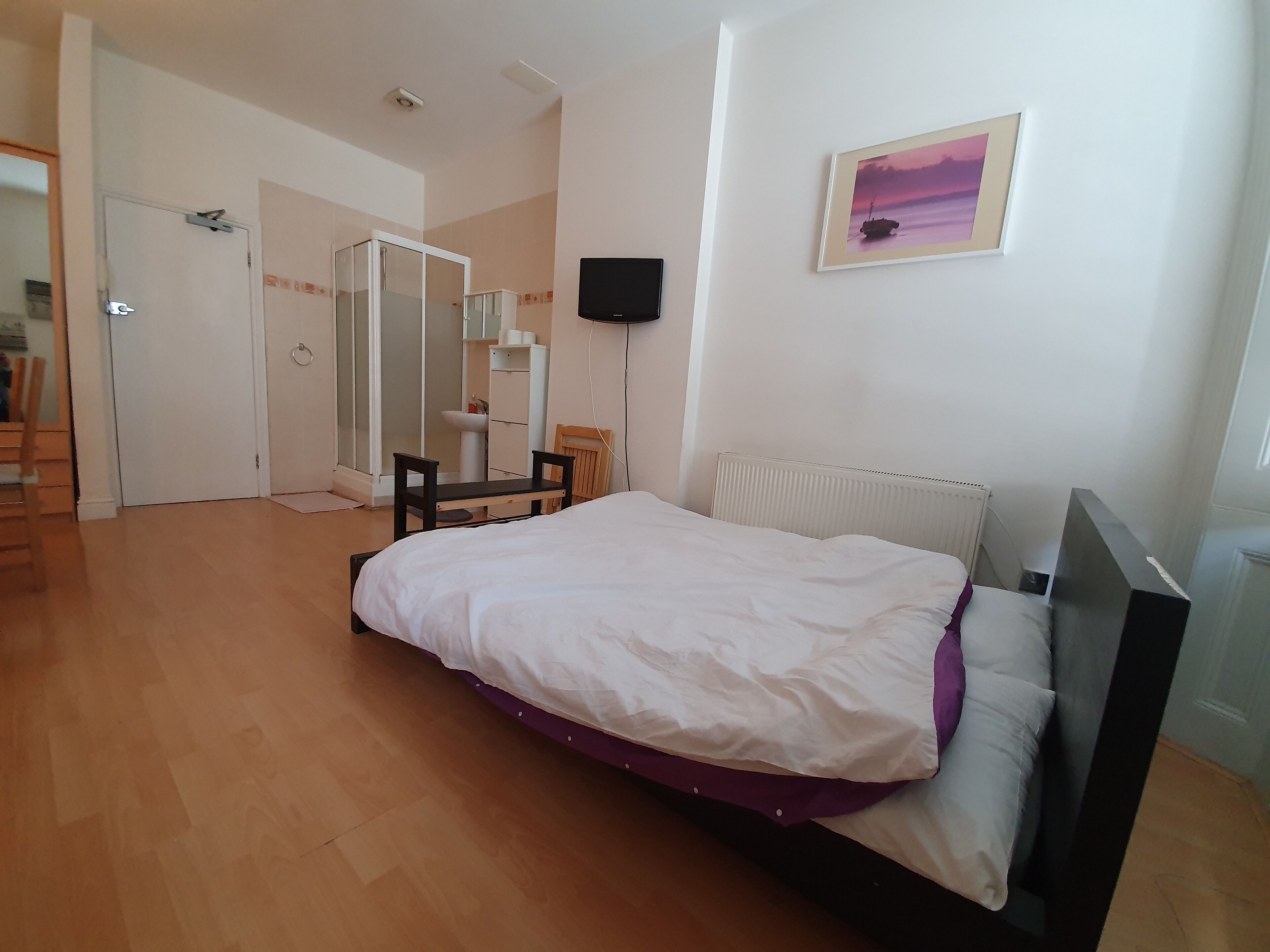 A bedroom with a bed, a mirror, a radiator, and a picture on the wall.