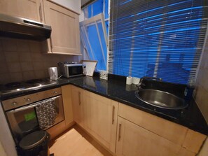 A compact kitchen with a stove, microwave, and sink. - Studio Apartment in South Kensington 15 (London)