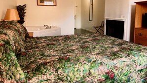 Un dormitorio con cama, lámpara de noche, un cuadro en la pared, baño con bañera y chimenea.