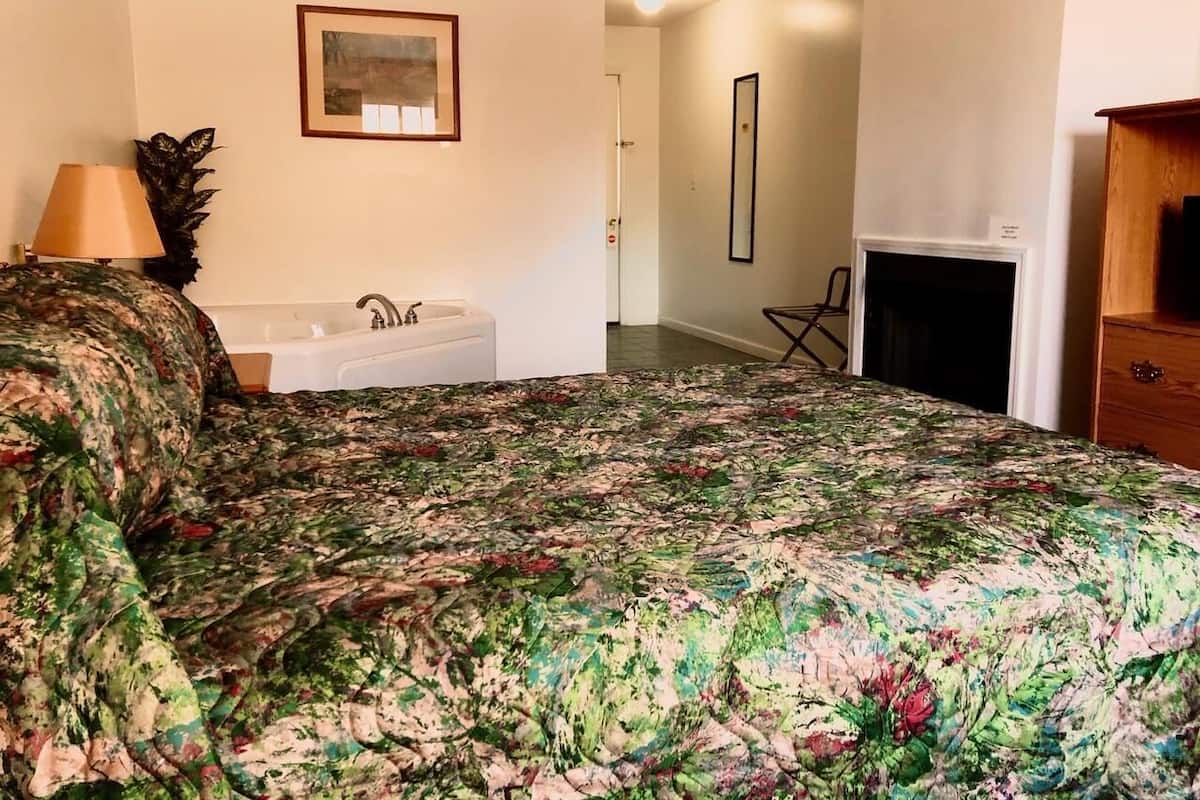Ein Schlafzimmer mit Bett, Nachttischlampe, einem Wandbild, einem Badezimmer mit Badewanne und einem Kamin.