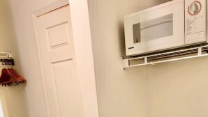 Una habitación con una puerta blanca, un microondas blanco montado en la pared y un congelador horizontal blanco.