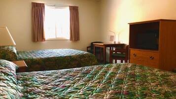 Habitación de hotel con dos camas, un escritorio, una silla, un televisor y una ventana con cortinas.