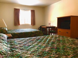 A hotel room with two beds, a desk, a chair, a television, and a window with curtains.