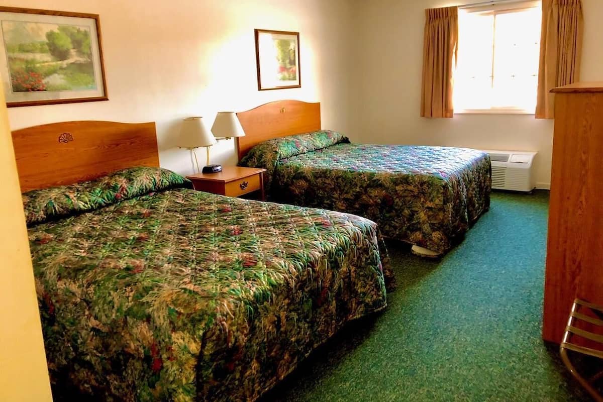 Ein Hotelzimmer mit zwei Betten, einem Nachttisch mit Lampe, einem Fenster mit Vorhängen und einem Bild an der Wand.