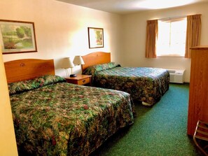 A hotel room with two beds, a nightstand with a lamp, a window with curtains, and a painting on the wall.