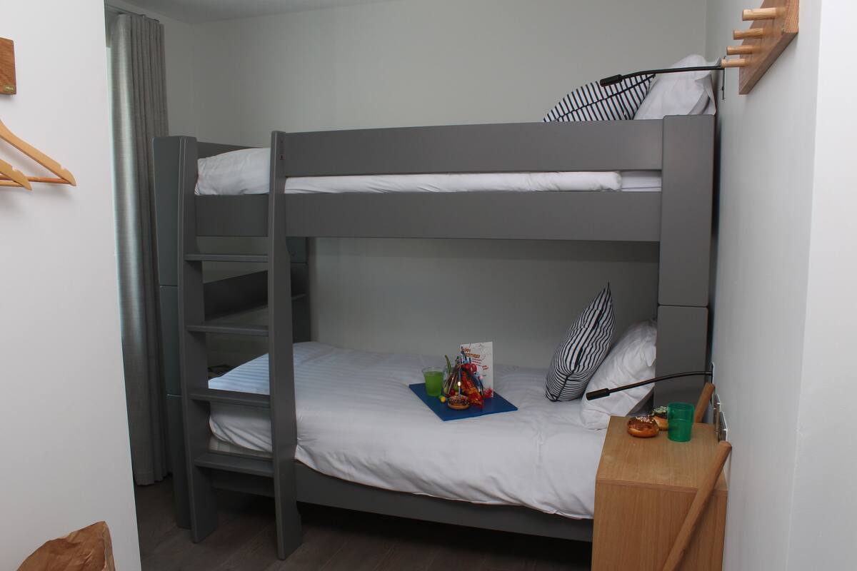 A bunk bed with a wooden side table, a green cup, and a striped pillow.