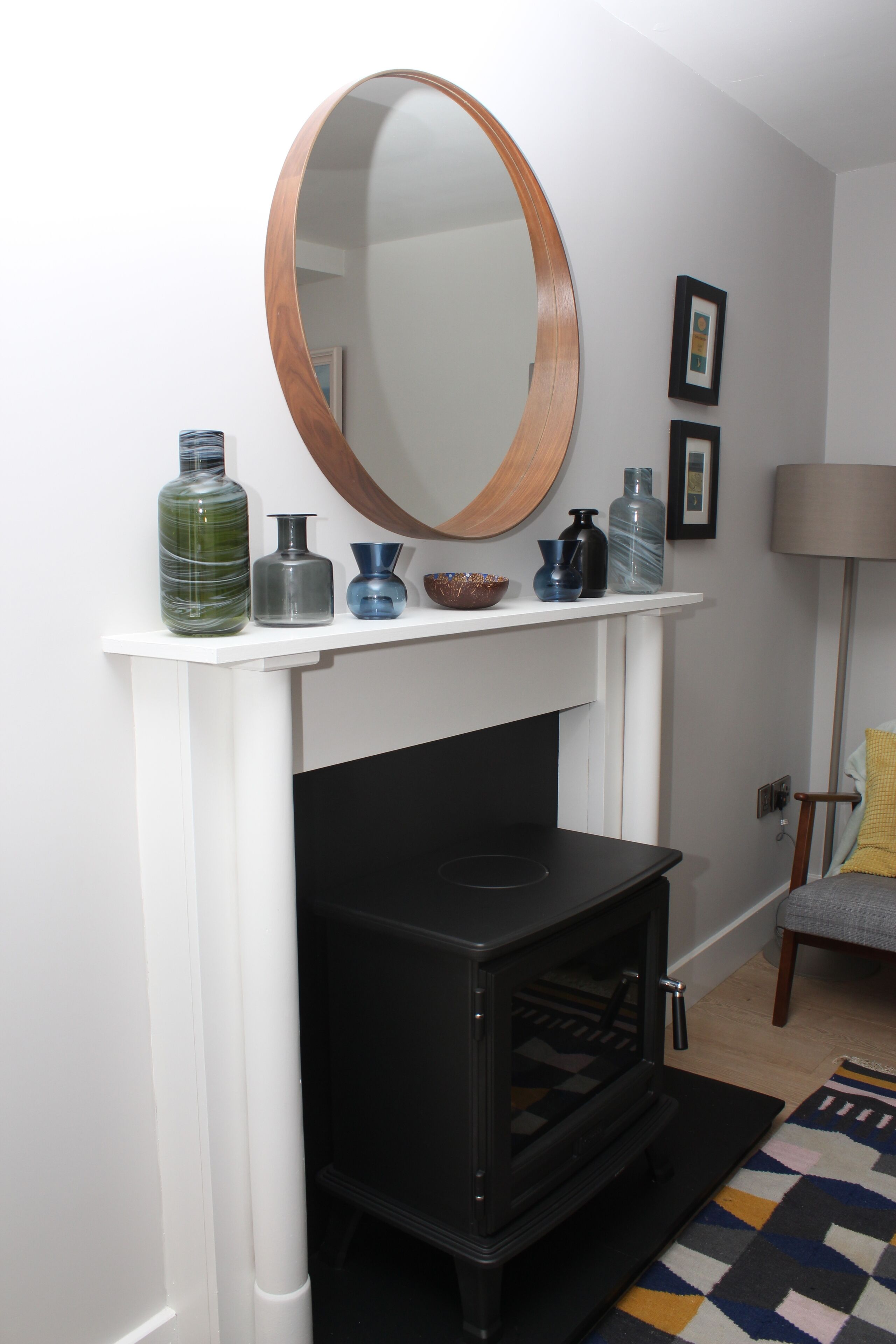 A modern living room with a white fireplace, a round mirror, and a shelf with decorative vases.