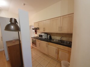 A kitchen with wooden cabinets, a microwave, a stove, a sink, and a floor lamp.