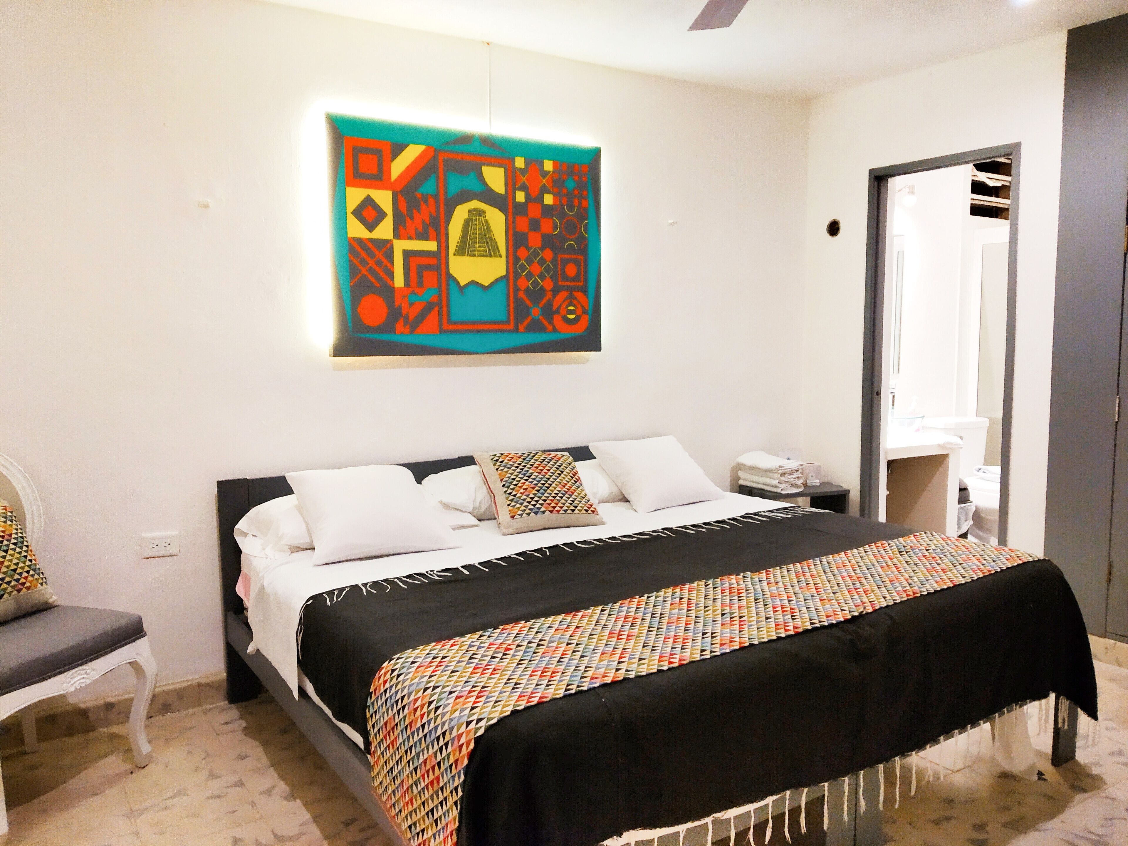 Un dormitorio con cama, una silla, una mesita de noche y una obra de arte colgada en la pared.