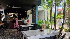 Een terrascafe met tafels en stoelen, een toonbank met etenswaren, en een decoratieve gitaar.