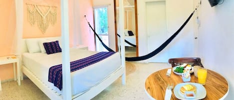 A room with a four-poster bed, a wooden dining table with breakfast, and a hammock.