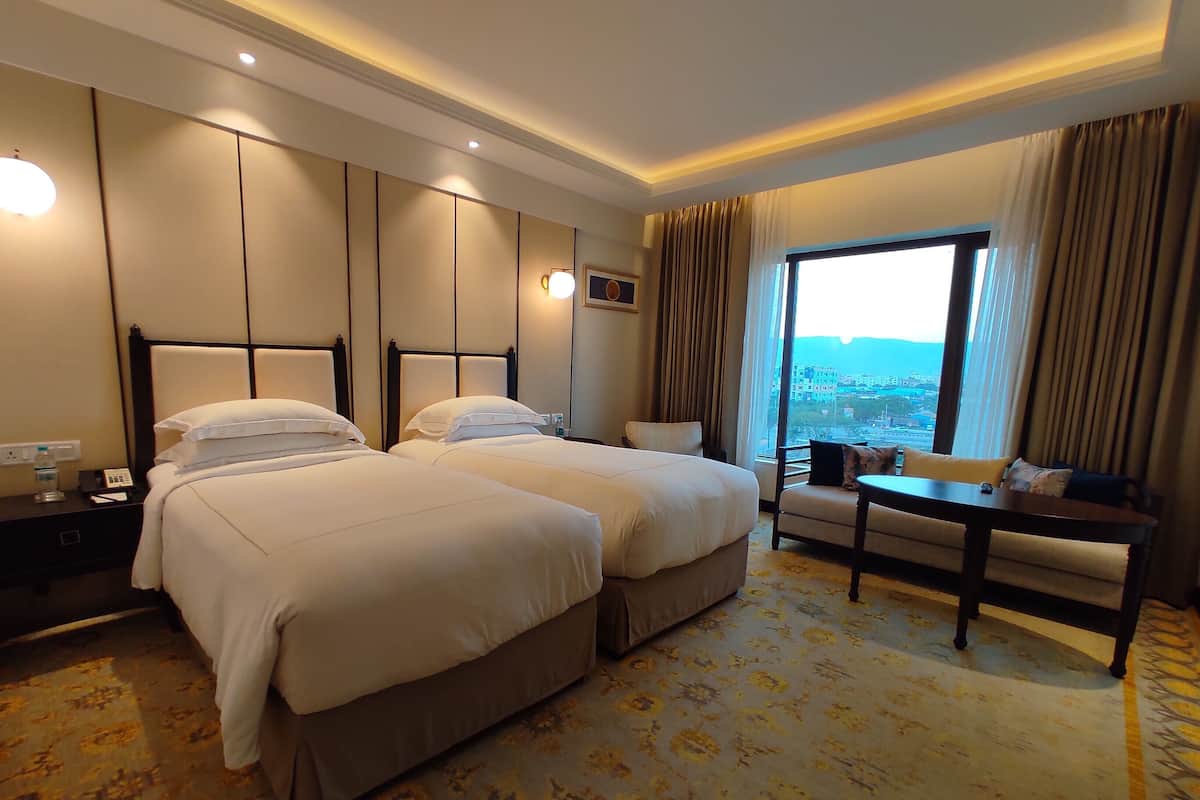 A hotel room with two beds, a desk, and a view of the city.