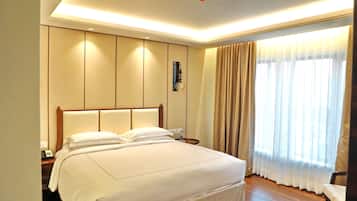 A hotel room with a large bed, a nightstand with a phone, and a window with curtains.