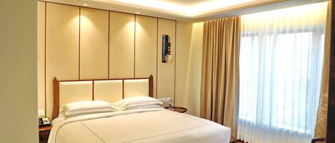 A hotel room with a large bed, a nightstand with a phone, and a window with curtains.