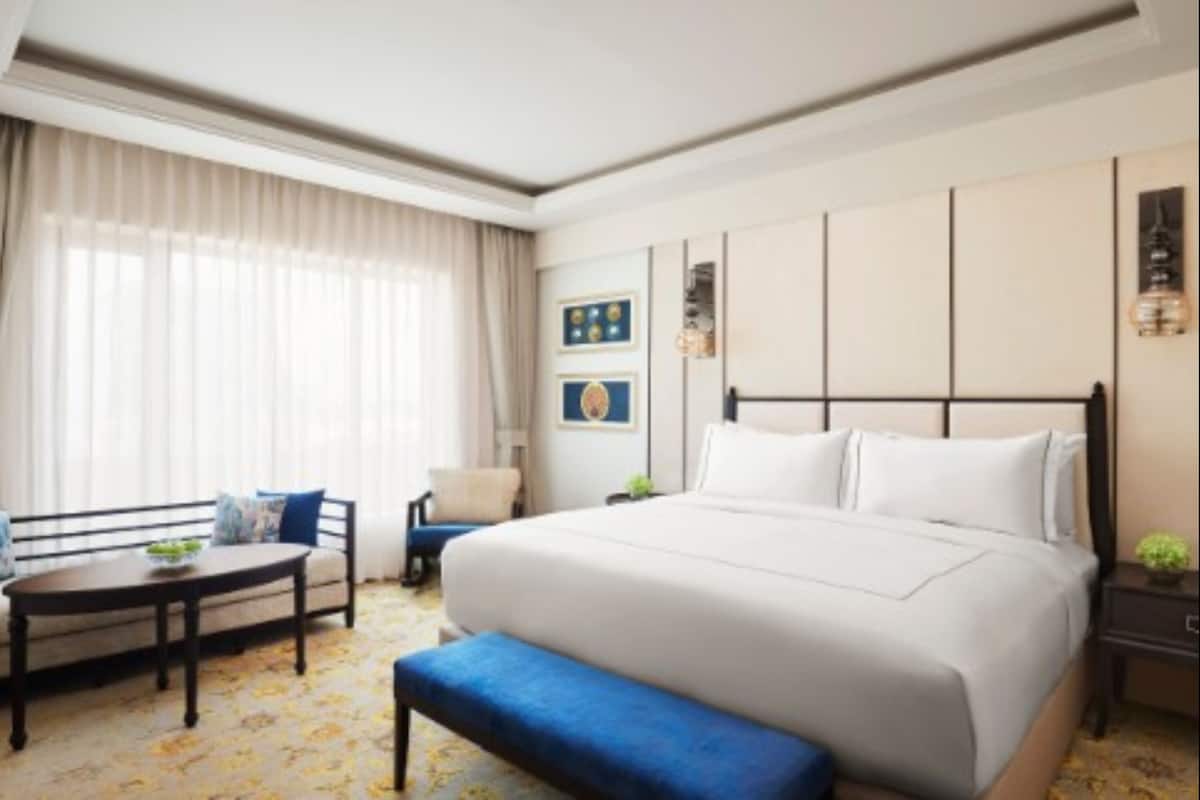 A hotel room with a large bed, a small table, a chair, and a bench.