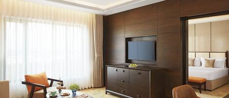 A hotel room with a bed, a TV on a cabinet, a dining table with chairs, and a large window with curtains.