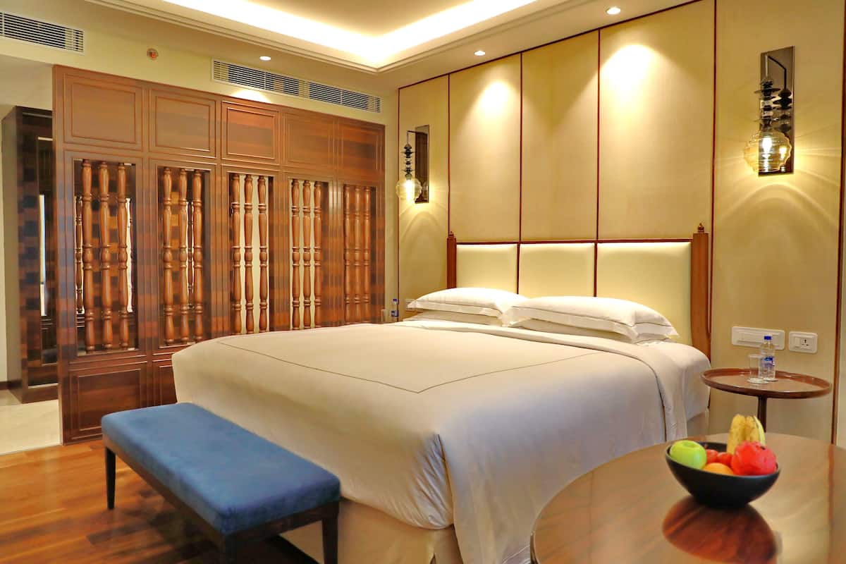 A hotel room with a large bed, a wooden wardrobe, a bench, and a small table with a fruit bowl.