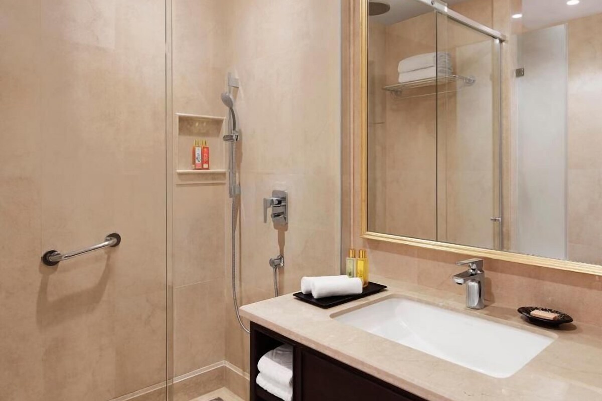A modern bathroom with a glass-enclosed shower, a large mirror, and a sink with toiletries.
