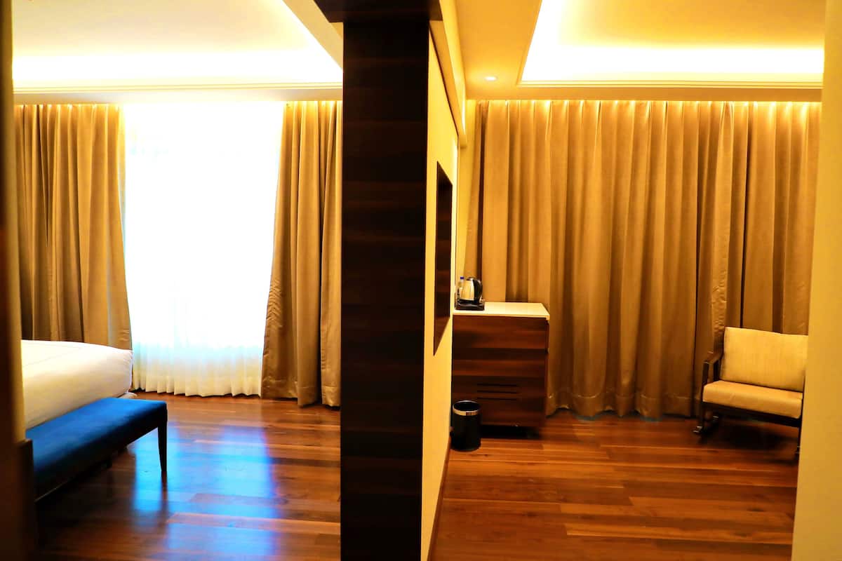 A hotel room with a bed, a bench, a small table with a kettle, and a chair.