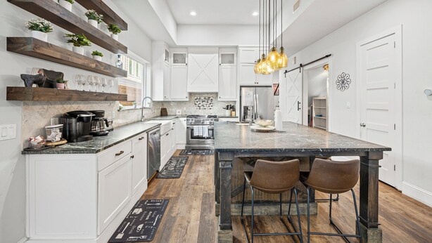 A modern kitchen with white cabinetry, wooden shelves, and a large island with bar stools.