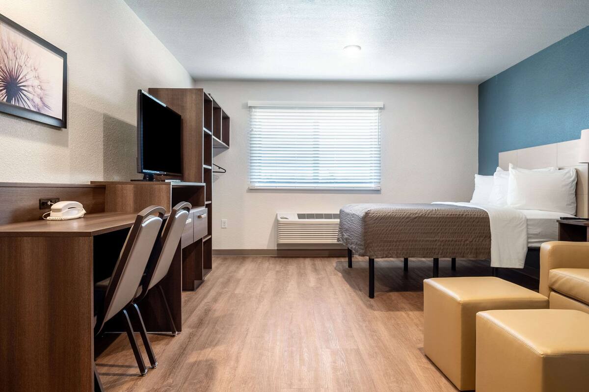A hotel room with a wooden desk, chairs, a bed, and a window with blinds.