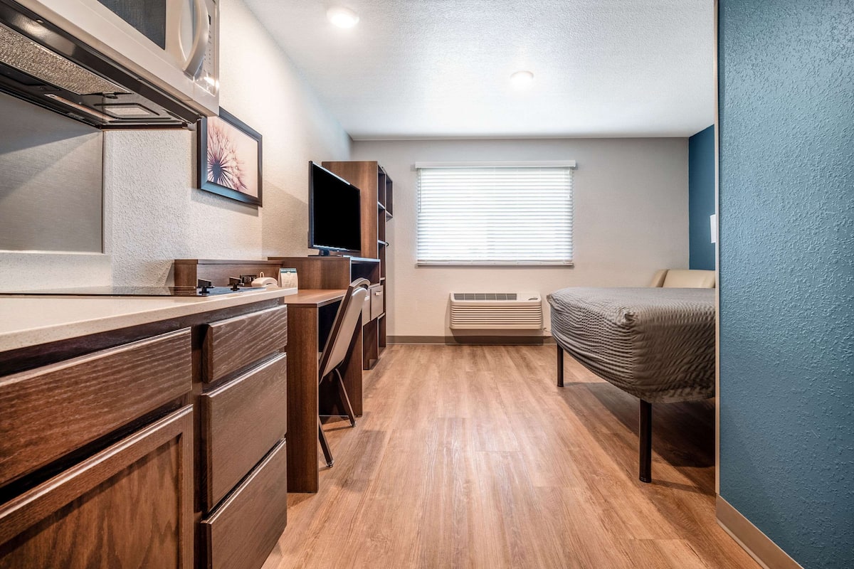 A compact kitchen with wooden cabinets, a built-in oven, and a window with blinds.