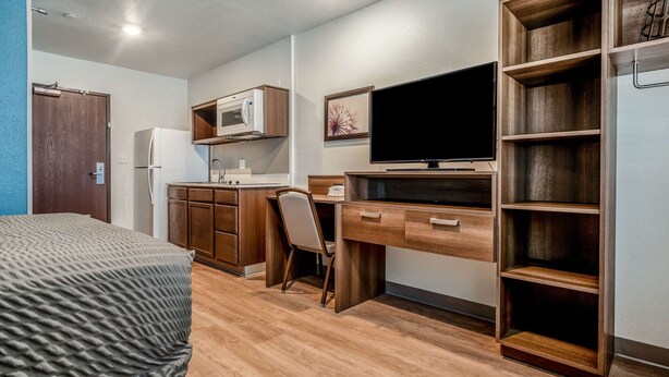 A compact room with a bed, a desk, a chair, a microwave, a TV, and a bookshelf. - WoodSpring Suites Naples West (Naples)