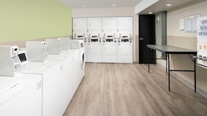 A laundry facility with multiple washing machines and dryers, a table, and a door leading to another room.