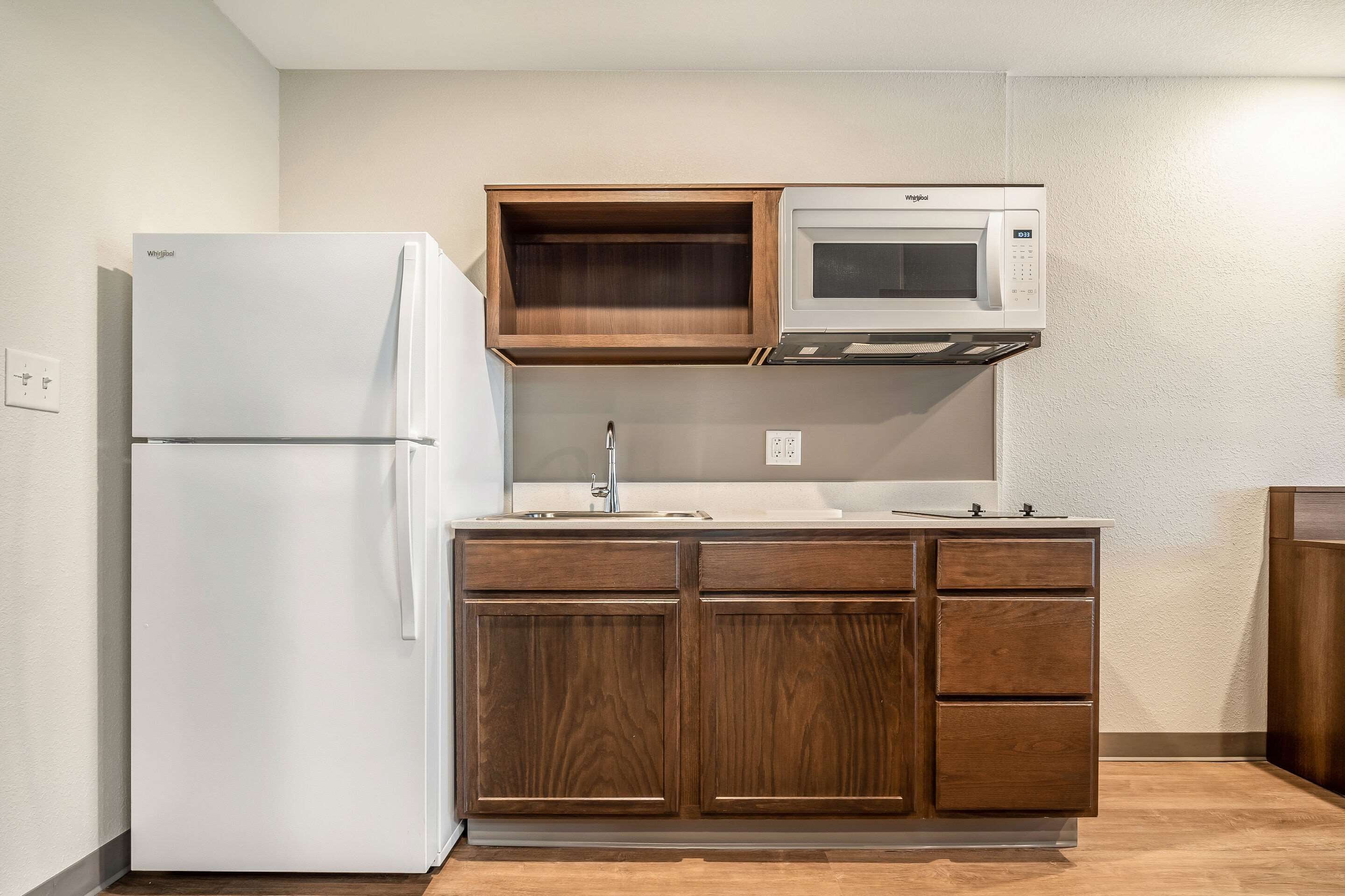 A compact kitchen with a white refrigerator, wooden cabinets, a microwave, and a sink.