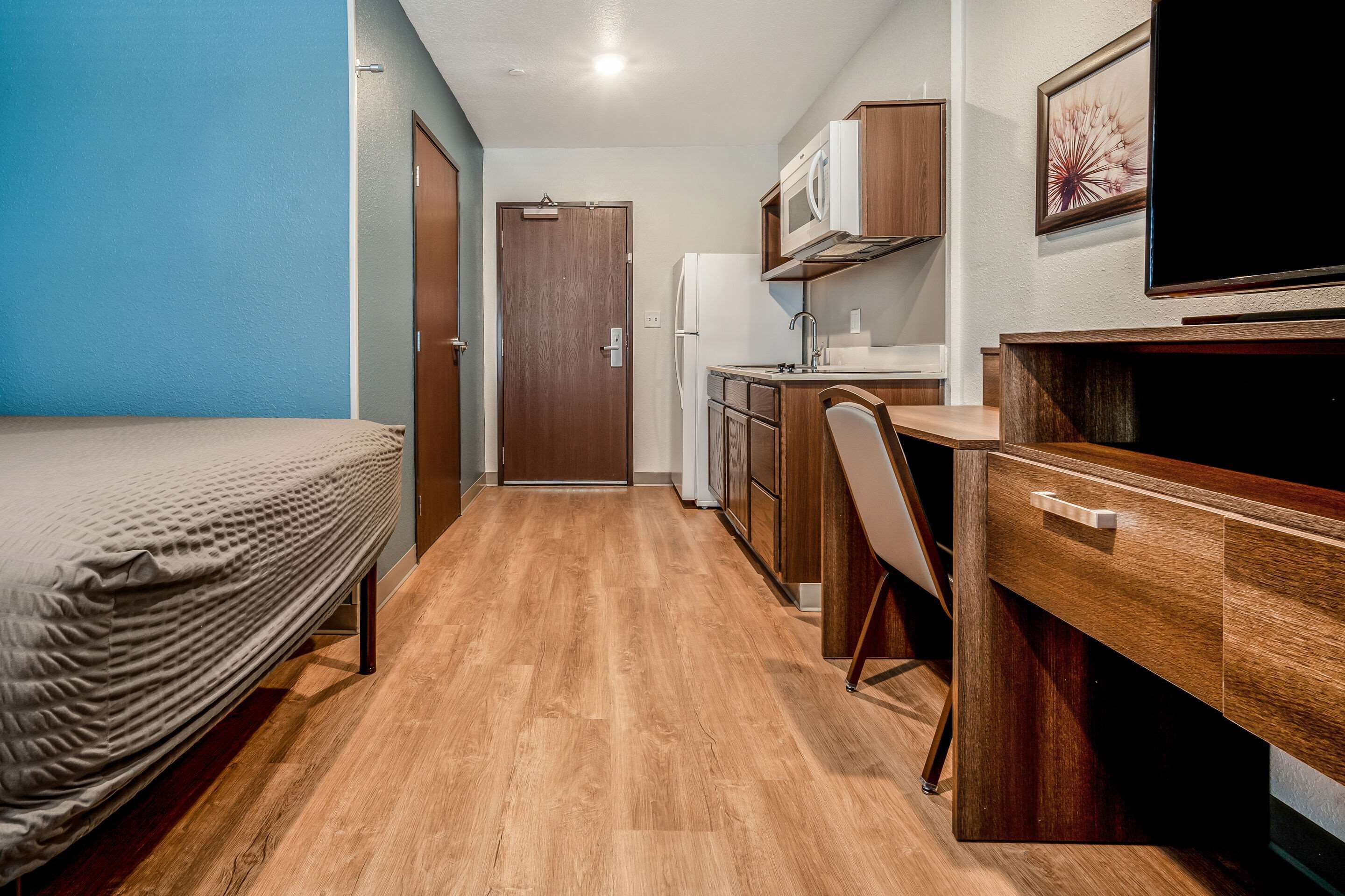 A compact room with a bed, a kitchenette, a desk, and a television.