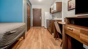 A compact room with a bed, a kitchenette, a desk, and a television.
