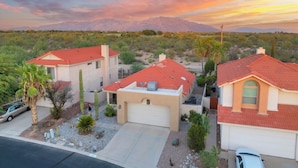 A residential area with two houses, each with a red roof and beige walls, surrounded by desert vegetation and mountains in the background. - Upscale Private Home In A Quite Gated Community With Breathtaking Mountain Views (Tucson)