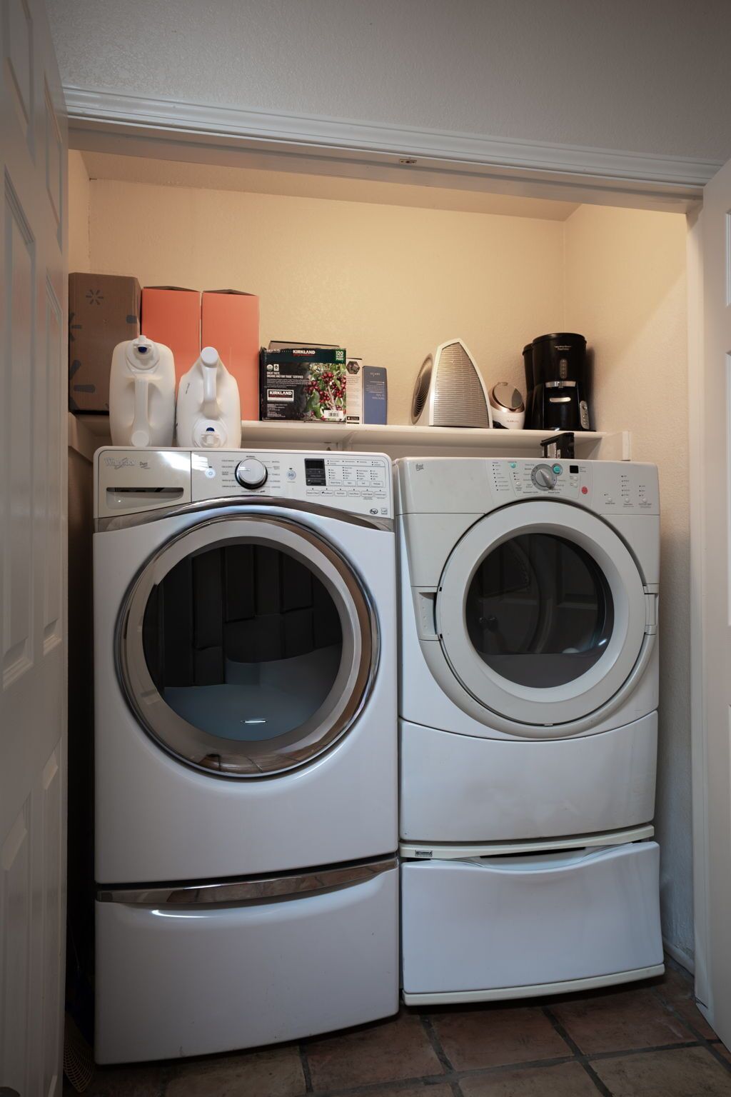 A laundry room with two stacked front-loading washing machines and a coffee maker on top.