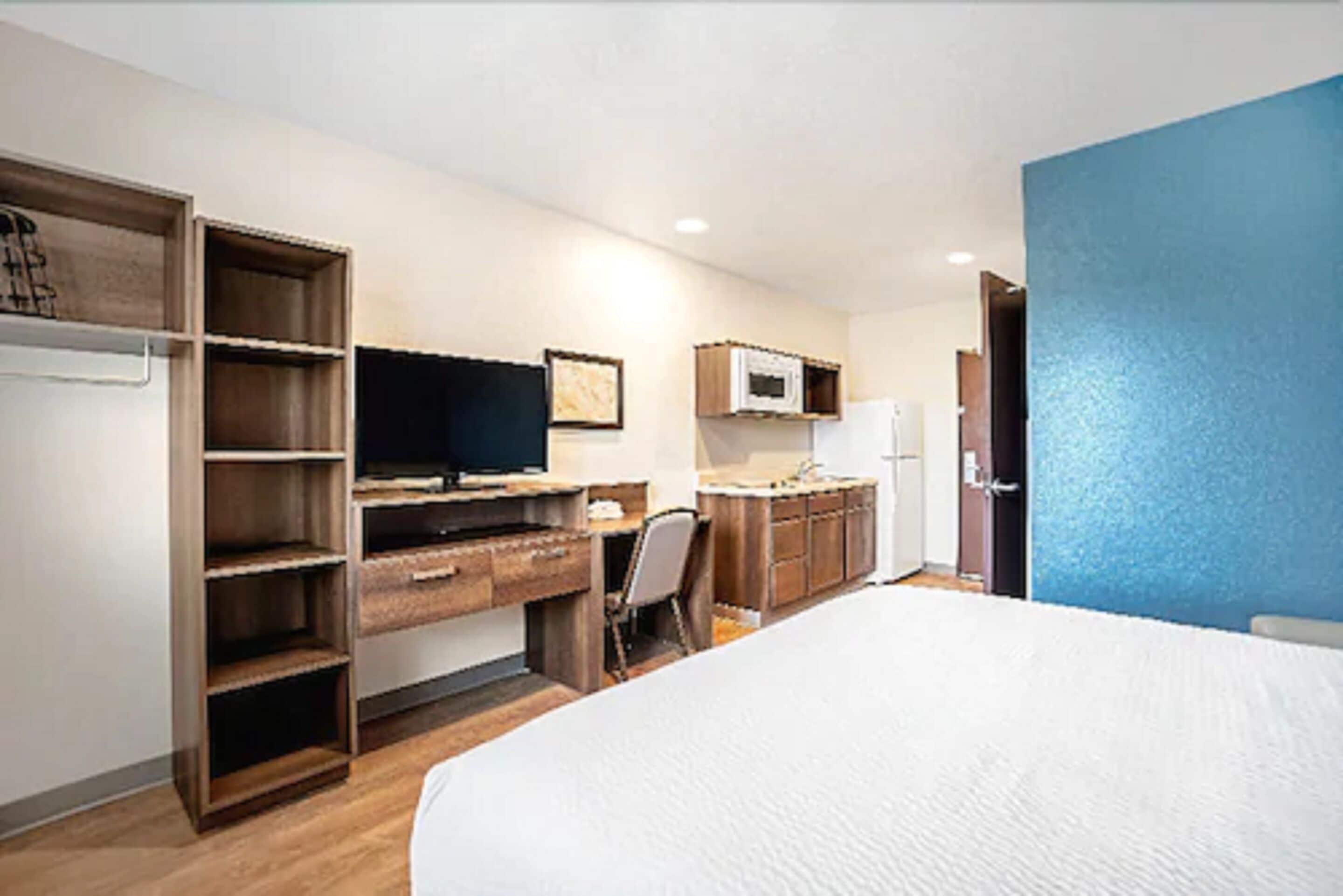 A hotel room with a bed, a desk with a computer, a chair, a wardrobe, and a microwave.