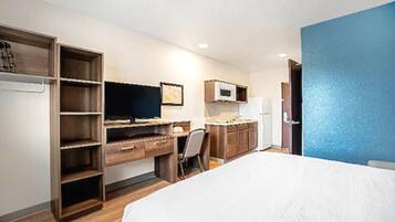 A hotel room with a bed, a desk with a computer, a chair, a wardrobe, and a microwave.