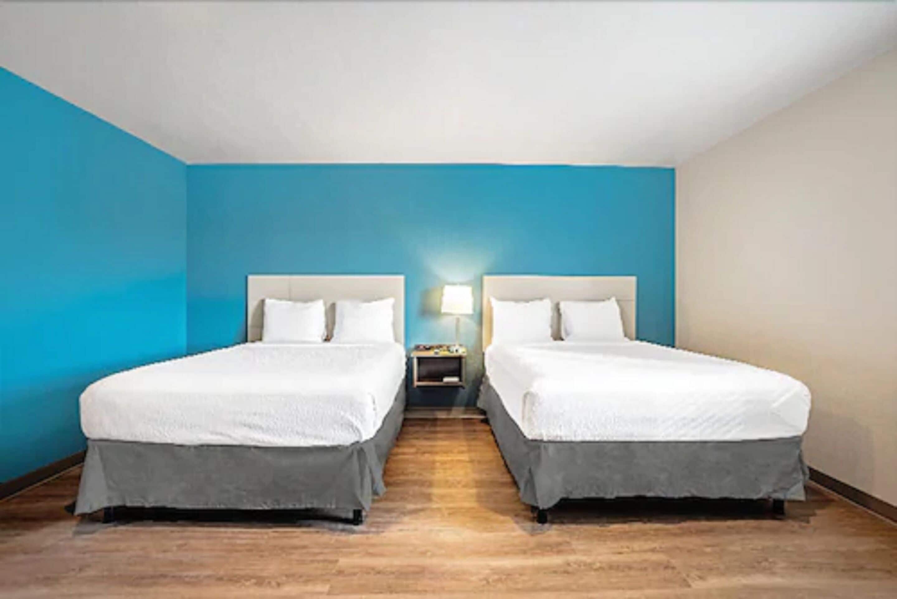 A hotel room with two beds, a nightstand, and a lamp.