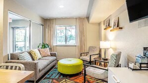 A modern living room with a sofa, ottoman, chairs, a coffee table, and a TV mounted on the wall. - WoodSpring Suites Tamarac (Tamarac)