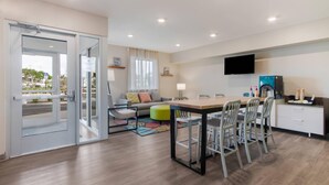 A modern hotel room with a dining area, a sofa, a TV, and a window with a view. - WoodSpring Suites Tamarac (Tamarac)