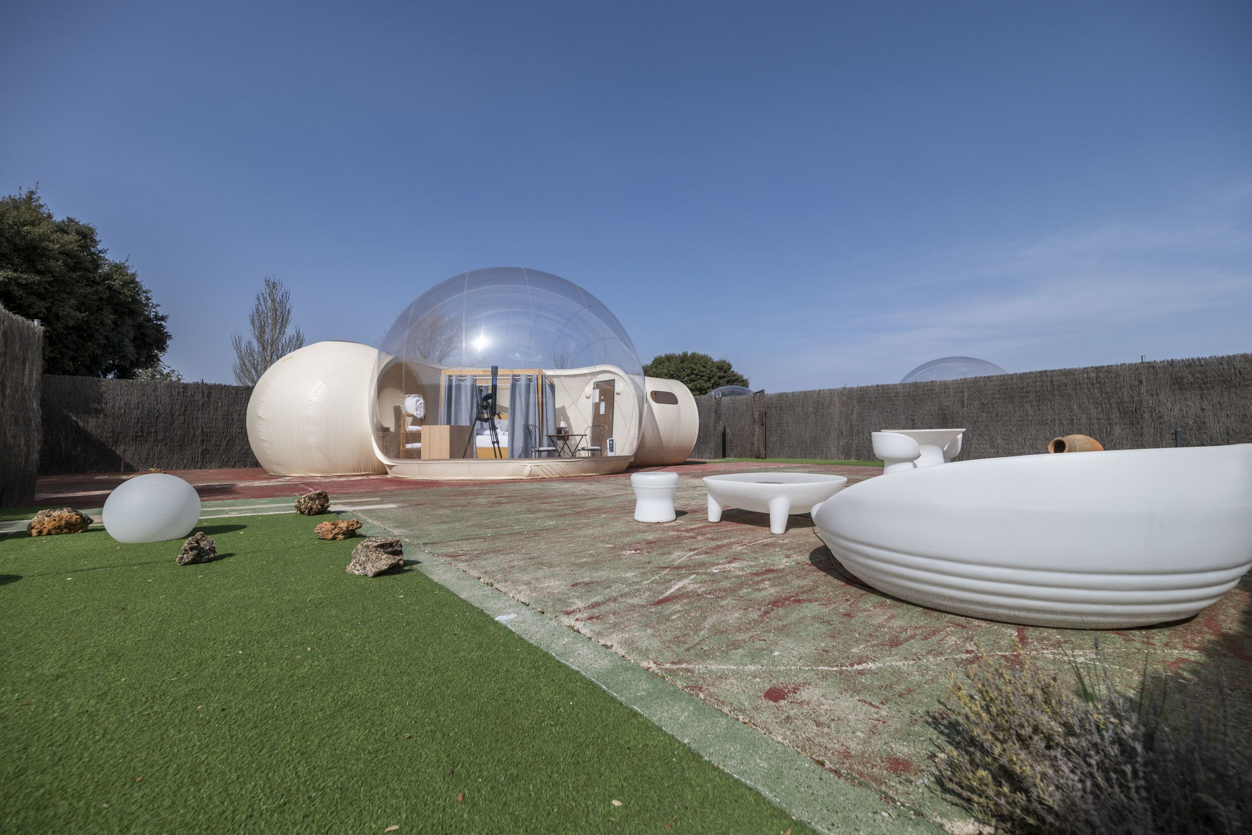 A transparent dome structure with a visible interior, surrounded by outdoor furniture and a green artificial turf area.