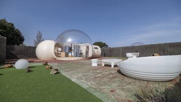 A transparent dome structure with a visible interior, surrounded by outdoor furniture and a green artificial turf area.
