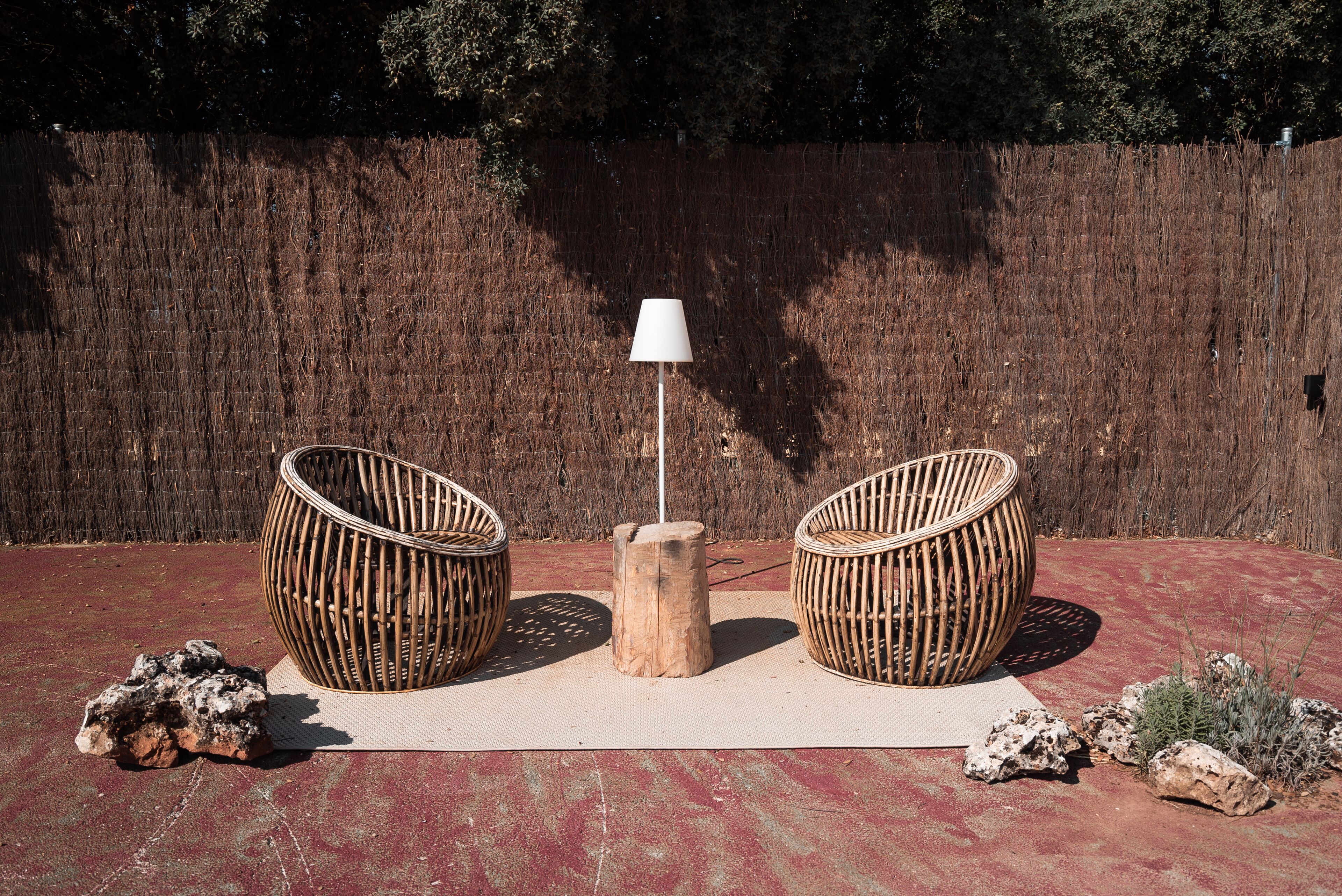 A seating area with two wicker chairs and a central wooden table with a white lamp.