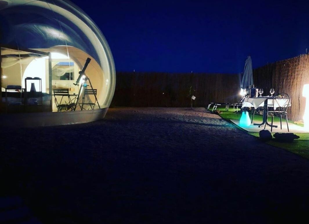 Una estructura abovedada con una mesa y sillas afuera, un telescopio y un coche estacionado cerca.