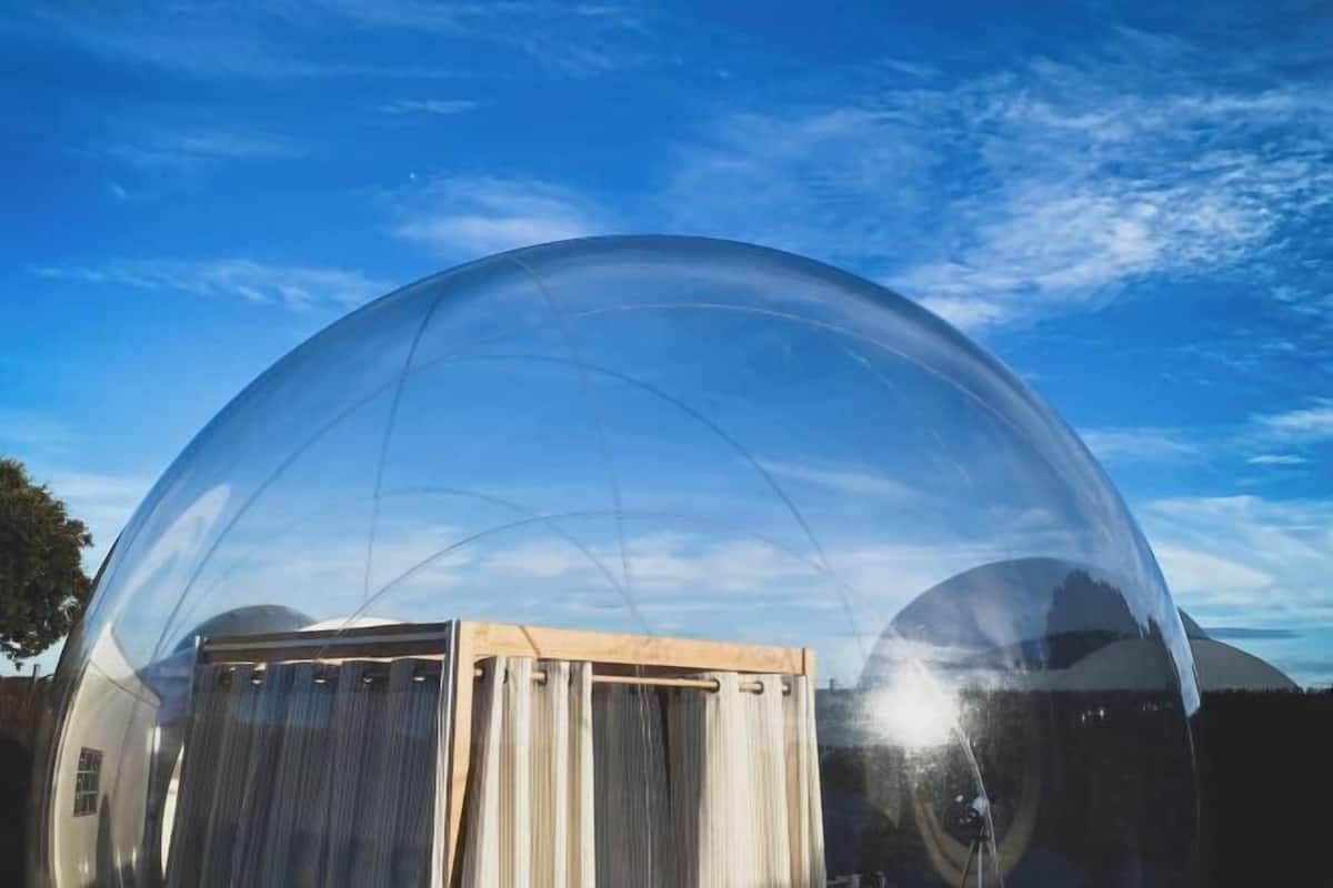 Una estructura con cúpula transparente sobre una base de madera, con cielo despejado de fondo.