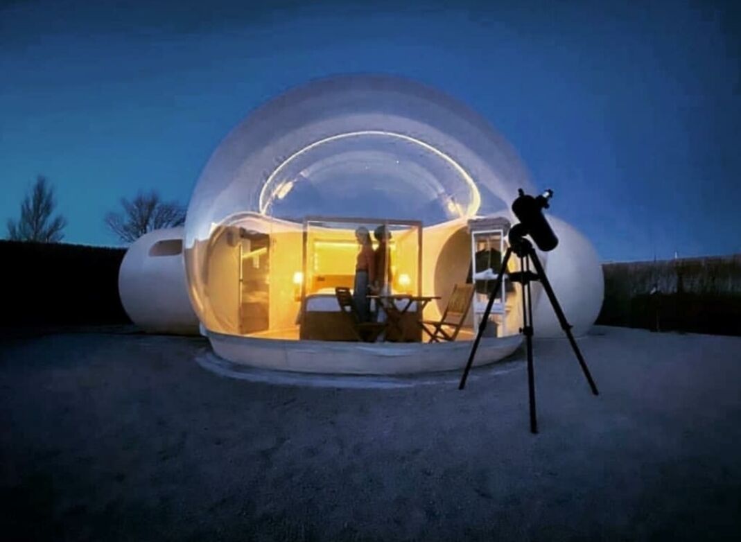 A geodesic dome structure with an interior seating area and a telescope on a tripod.