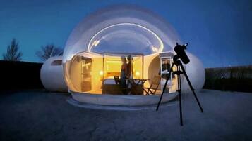 A geodesic dome structure with an interior seating area and a telescope on a tripod.